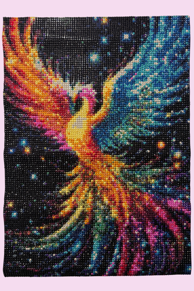Project – Firebird Completed diamond painting of a colourful firebird with outstretched wings in shades of orange, red, pink and turquoise, surrounded by sparkling stars against a dark background.