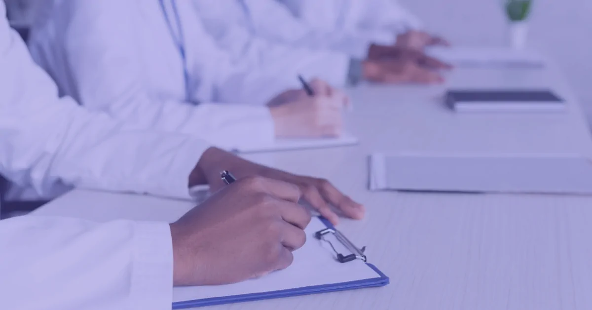 Doctors Taking Notes During a Medical Consultation Meeting Doctors in white coats writing notes on clipboards at a conference table.