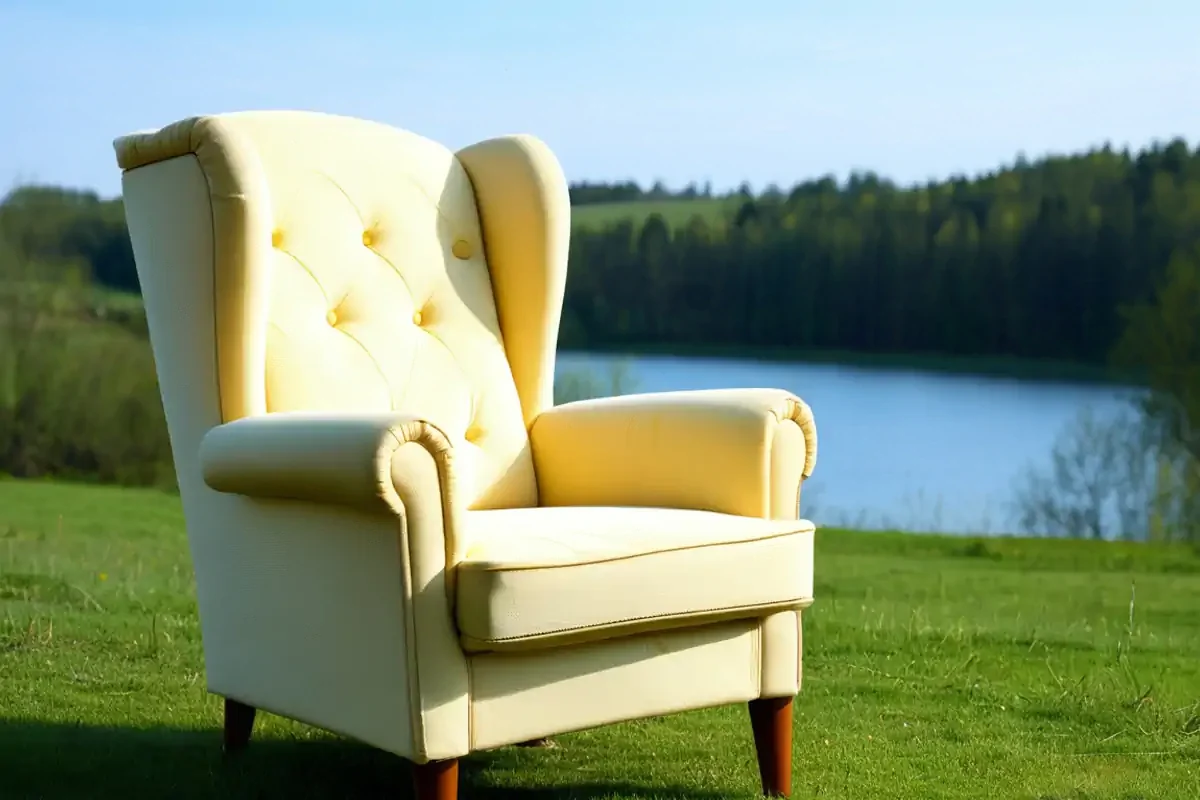 A photo of an armchair sat in the middle of the countryside with a lake behind.