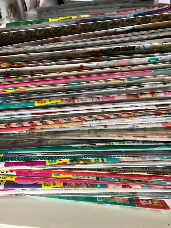 Tall pile of vibrant craft magazines with floral, patterned covers – endless low-energy project ideas for fibromyalgia flare-ups.